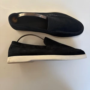 Svarta mockaloafers med vit sula - Snygga marinblåa loafers i mocka med vit platt gummisula. Skorna har en klassisk, stilren design med rund tå och diskreta sömmar längs ovansidan. Storlek 42