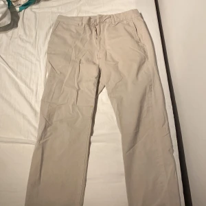 Beige chinos från Kappahl W32 L34 - Snygga beige chinos från Kappahl i klassisk rak modell. Byxorna har fickor fram och bak, bälteshällor och stängs med knapp och dragkedja. Perfekta för en clean och stilren look.