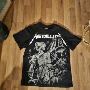 Svart Metallica t-shirt Lucky Boy S - Svart t-shirt med Metallica-tryck fram och stort logomotiv bak. Framsidan har motiv från '...And Justice For All' med Lady Justice och bandets logga. Litet hål vid ena armen, därav lägre pris