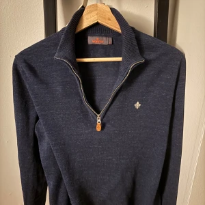 Marinblå half zip-tröja från Morris - Snygg marinblå stickad tröja från Morris med half zip och ribbad krage. Tröjan har lång ärm och en liten broderad logga på bröstet. Perfekt för lager-på-lager och chill stil.