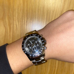 Silverfärgad HUGO BOSS kronografklocka - Stilren klocka från BOSS i silverfärgat rostfritt stål med svart urtavla och tre mindre subdials. Länkar i metall och tydlig BOSS-logga på spännet. Klockan har sportig känsla med tachymeter runt urtavlan och robust design. Perfekt accessoar för dig som gillar klassisk stil.