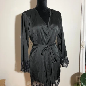 Svart morgonrock med spets - Svart kort morgonrock med spets och knytning i midjan. Längd ca 80cm. Ärmlängd ca 60cm. Pris: 10kr 