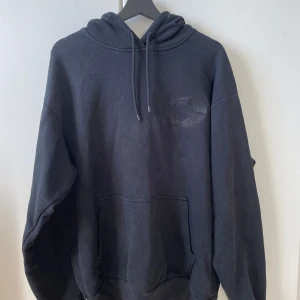 Svart oversized hoodie från Gasp  - Svart hoodie från Gasp med broderad logga på bröstet. Oversized passform, huva med snörning och stor magficka framtill. Perfekt för dig som gillar streetwear och Gym