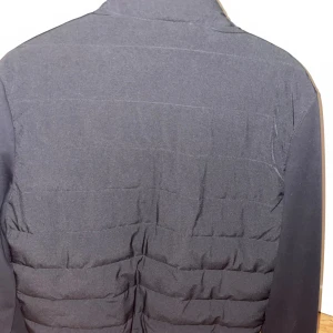 Svart cardigan med dragkedja - Stilren svart cardigan med quiltad design och hel dragkedja framtill. Jackan har en rundad krage och raka ärmar. Perfekt för dig som gillar en clean look och vill ha en jacka som funkar till många outfits,(från Zara.) org pris 450kr