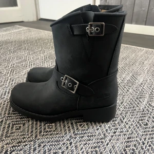 Svarta Johnny Bulls boots i skinn - Säljer ett par svarta boots från Johnny Bulls i äkta skinn. Modellen har rund tå, platt sula och två snygga spänndetaljer i silver. Insidan är ljus och mjuk, och yttersulan är rejält mönstrad för extra grepp. Aldrig använda. 
