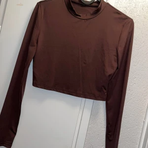 Croptop  - Snygg brun croppad polotopp med lång ärm. Toppens material är mjukt och stretchigt, perfekt för att styla med höga jeans eller kjol. Enkel design utan mönster eller detaljer, med en liten polokrage som ger en clean och modern look. Aldrig kommit till användning