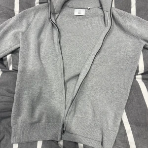 Grå kofta med dragkedja från Bläck - Snygg grå kofta från Bläck i mjuk bomullsmix. Tröjan är köpt nu i somras men ej kommit till användning mer än två tre gånger då den sitter litet på mig, köpt för 899 säljes för 549