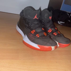 Svarta Jordan basket sneakers - Säljer ett par svarta Jordan basket sneakers med röda och vita detaljer. Skorna har högt skaft, snörning och den klassiska Jumpman-loggan på plösen. Sulan är vit med röd undersida och skon har coola röda detaljer på snörningen. Perfekta för dig som gillar basket och streetstyle.