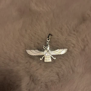 Silverfärgat Faravahar-halsband - Unikt halsband med en detaljrik Faravahar-symbol i silverfärg. Hängsmycket har snygga linjer och en cool, stilren look. Perfekt för dig som gillar persisk kultur och vill ha något speciellt runt halsen.