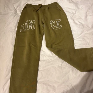 Tuttolente  - Olivgröna tuttolente byxor med vita broderade bokstäver på framsidan. Byxorna har resår i midjan och snörning för extra komfort. Tillverkade i mjukt material som passar perfekt för chill dagar. Snygg och avslappnad passform.