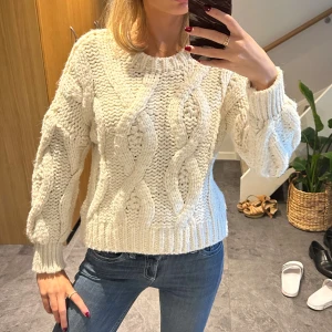 Vit chunky stickad tröja från - Säljer denna supermysiga vita stickade tröjan med grovt flätmönster. Tröjan har rund hals, långa ärmar och ribbade muddar. Perfekt för kyliga dagar och ger en riktigt cozy vibe till din outfit.