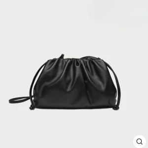 Svart axelväska med snörning - Snygg svart axelväska i slätt skinnimitation med cool snörningsdetalj upptill. Väskan har en mjuk, puffig form och smal axelrem som gör den enkel att bära. Perfekt för dig som gillar minimalistisk och trendig stil. Aldrig använt och är helt som ny❣️❣️