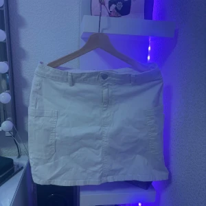 Vit jeanskjol från Unique You - Vit kort jeanskjol från Unique You Unique Denim i storlek M. Kjolen har två stora fickor framtill, bälteshällor och klassisk knappstängning. Perfekt för dig som gillar en enkel och clean stil.