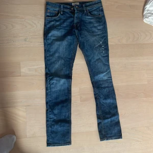 Mörkblå jeansbyxor straight fit - Snygga mörkblå jeansbyxor med klassisk femficksdesign och raka ben. Jeansen har slitningar på låret och en diskret tvättad look som ger en cool vibe. Perfekta för dig som gillar en enkel men stilren stil.