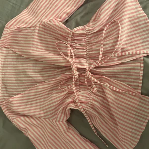 Rosa och vit randig blus med snörning - Säljer en söt blus med rosa och vita ränder. Toppen har långa ärmar och snygg snörning framtill som ger en unik look. Luftigt material, perfekt för varmare dagar. Passformen är normal och toppen har en lätt croppad känsla.