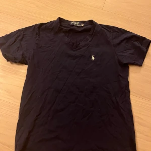 Svart v-ringad t-shirt från Polo - Svart t-shirt från Polo i 100% bomull med v-ringning och korta ärmar. Klassisk broderad logga på bröstet i vitt. Enkel och stilren modell som passar perfekt till jeans eller shorts.