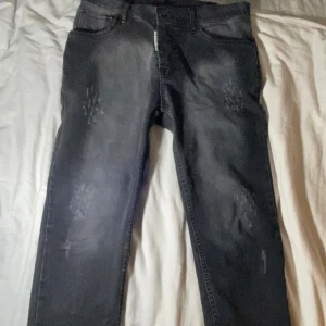 Grå Dsquared2 jeans ICON - Snygga grå jeans från Dsquared2 med ICON-lapp bak och diskreta slitningar framtill. Jeansen har en rak passform, klassiska fem fickor och dragkedja. Perfekta för dig som gillar streetstyle och vill sticka ut med en exklusiv look. Äkta!!