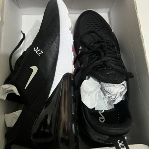 Nike Air Max 270 svarta sneakers - Nike Air Max 270 sneakers i svart med vit sula och tydlig Air Max-bubbla i hälen. Ovandelen är i mesh och syntet, med vita Nike-loggor och 270-detaljer på sidan. Skorna har snörning och en sportig, modern look som passar perfekt till streetwear. De är helt nya de va för stora bara 