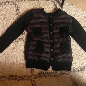 Svart jacka med stickade ärmar - Säljer en snygg svart jacka från Cacharel i storlek M. Den har en quiltad framsida med knappar och stickade ärmar. Perfekt för höst och vår när du vill ha något stilrent och bekvämt. Två praktiska fickor framtill. Passar både till vardags och lite finare!💗💗