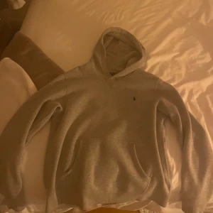 Grå hoodie från Ralph Lauren - Klassisk grå hoodie från Polo Ralph Lauren i storlek XL men liten i storleken!!!! Skulle säga motsvarar s-m. Tröjan har huva, magficka och den ikoniska lilla broderade loggan på bröstet. Mjuk insida och långärmad modell, perfekt för chill dagar. Enkel och stilren design som funkar året runt. Köpt på kidsbrandstore. Finns ett litet hål på ärmen men inget som syns jättetydligt. Hör av er vid funderingar❤️