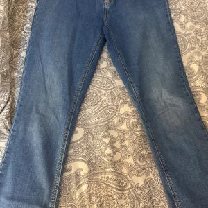 Blå bootcut jeans med rå kant - Snygga blå jeans med bootcut passform och rå, ofållad kant längst ner. Klassisk denim med kontrastsömmar i gult och en stilren look. Perfekta för dig som gillar en avslappnad men trendig stil.