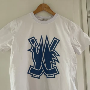 Vit Moncler t-shirt med blått tryck - Snygg vit t-shirt från Moncler med stort blått grafiskt tryck på bröstet och klassisk logga på ärmen. Skön passform och tillverkad i mjuk bomull. Perfekt för dig som vill ha en clean men ändå unik look.