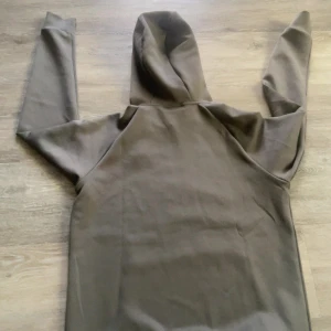 Mörkgrå hoodie med huva - Säljer en stilren mörkgrå hoodie med huva och magficka. Tröjan har långa ärmar och en klassisk passform, perfekt för chill dagar. Materialet känns mjukt och skönt mot huden. Enkelt och snyggt plagg som funkar året runt.