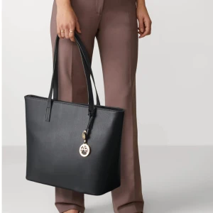 Svart axelväska från Michael Kors - Stilren svart axelväska från Anna Fielde i slät skinnimitation med raka linjer och långa handtag. Perfekt storlek för att få plats med allt du behöver och passar till många olika looks. Helt ny!