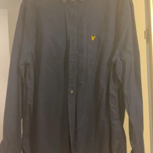 Mörkblå skjorta från Lyle & Scott  - Mörkblå skjorta från Lyle & Scott i bomull med klassisk krage och knappar hela vägen. Väldigt liten i storlek passar M/L