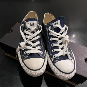 Converse All Star navy låga sneakers - Klassiska Converse All Star sneakers i marinblå canvas med vita snören och gummitå. Låg modell med vit sula och bruna detaljer undertill. Helt oanvända och skickas i orginal förpackning.