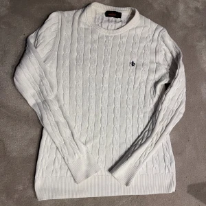 Vit kabelstickad tröja Morris XS - Vit kabelstickad tröja från Morris i storlek XS. Klassisk modell med rund halsringning, ribbade muddar och diskret broderad logga på bröstet. Perfekt för dig som gillar stilrena och tidlösa plagg. Plagget är i mycket fint skick och det är bara att fråga vid funderingar! Pris ej hugget i sten