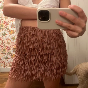 Rosa franskjol med volym - Supersnygg kort kjol i dammigt rosa med massor av fransar som ger en cool och lekfull look. Kjolen har en rak passform och är perfekt för dig som vill sticka ut. Materialet känns mjukt och följsamt, och fransarna ger extra rörelse till outfiten.