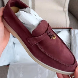 Vinröda mockaloafers med gulddetalj - Snygga vinröda Loro Piana loafers i mocka med en stilren gulddetalj framtill. Skorna har en platt, ljus sula och klassisk rund tå. Perfekta för dig som vill ha en dressad men avslappnad look.