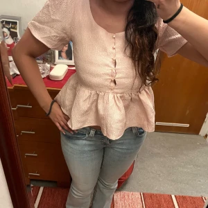 Ljusrosa blus med volang och knappar - Supersöt ljusrosa blus från H&M med korta puffärmar, volang nertill och dekorativa knappar framtill. Storlek S och använd endast en gång!! 💗💗💗