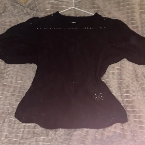 Svart blus med broderade detaljer - Säljer en svart blus med broderade hål och puffiga korta ärmar. Blusen har rund halsringning och ett feminint, luftigt tyg med fina detaljer. Perfekt för dig som gillar en stilren men ändå unik look.