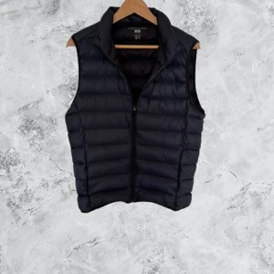 Svart dunväst från Uniqlo  - Svart, lätt och quiltad dunväst från Uniqlo Ultra Light Down. Västen har en klassisk ståkrage, dragkedja framtill och horisontella sömmar. Perfekt för lager-på-lager och enkel att bära med sig tack vare den smidiga designen.