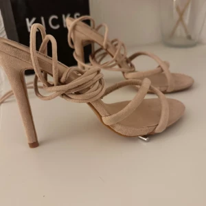 Beige sandaler med snörning från Boohoo - Snygga beige sandaler från Boohoo med höga klackar och trendig snörning runt vristen. Skorna har öppen tå, tunna remmar och är gjorda i mockaliknande material. Perfekta för att lyfta din outfit 