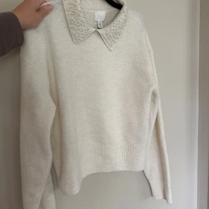 Vit stickad tröja med pärlkrage H&M - Superfin vit stickad tröja från H&M med lång ärm och en snygg krage dekorerad med pärlor. Tröjan har en rak passform och ribbade muddar vid ärmslut och nederkant. Perfekt för dig som vill ha något stilrent men ändå extra.