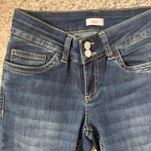 Blå bootcut jeans från Nelly - Ny utan prislapp!! Blå bootcut jeans från Nelly med låg midja och femficksdesign. Jeansen har kontrastsömmar, dubbla knappar i midjan och dekorativa sömmar på bakfickorna. Nypris 699kr!