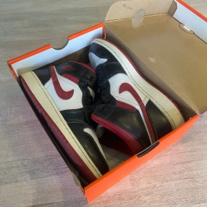 Nike Air Jordan 1 Gym Red  - Säljer ett par klassiska Nike Air Jordan 1 i svart, rött och vitt. Skorna har högt skaft, snörning och den ikoniska swoosh-loggan i rött på sidorna. Perfekta för dig som gillar streetstyle och vill sticka ut med en tidlös sneaker.