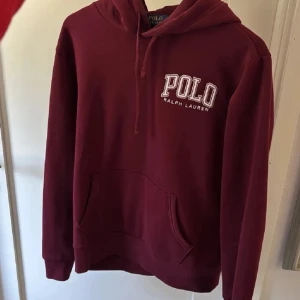 Vinröd hoodie från Polo Ralph Lauren - Snygg vinröd hoodie från Polo Ralph Lauren med broderad logga på bröstet. Tröjan har huva med snörning, känguruficka och långa ärmar. Perfekt för dig som gillar klassisk streetstyle och vill ha något bekvämt och stilrent.