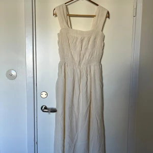 Ljus midiklänning från H&M - Superfin klänning från H&M i ljus beige färg. Klänningen har breda axelband, smockad överdel, luftigt tyg och underkjol, därav ej genomskinlig. Oanvänd, prislappen kvar. Passar xs/s pga stretchen i smockade överdelen. 