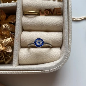 Silverring med blå och vita stenar. - Snygg silverfärgad ring med rund topp dekorerad med blå och vita stenar i ett blommigt mönster. Perfekt för dig som vill ha en färgklick på handen och gillar klassisk men ändå unik design.