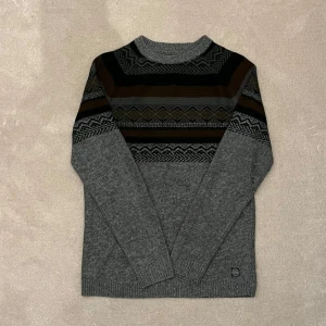 Stickad grå mönstrad tröja - Snygg grå tröja med ett stilrent mönster i svart och brunt över bröstet och axlarna. Vid minsta fråga eller fundering hör av er🤝