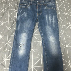 Blå jeans från Dsquared2, 14Y - Snygga blå jeans från Dsquared2 köpte dom från minto ny pris va runt 3 tusen köpte dom på rabbat så tror de va typ 4 tusen dom skulle kosta och dom har slitna detaljer och coola slitningar framtill. Klassisk femficksmodell med knappgylf och Dsquared2-logga på röd etikett. Jeansen är lite stretch för skön passform.