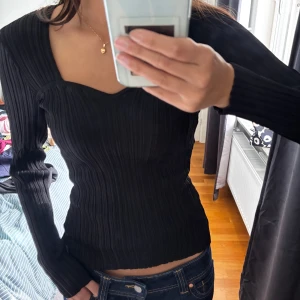 Svart ribbad topp från H&M XS - Svart långärmad topp från H&M i storlek XS. Toppen har en snygg v-ringad skärning och är ribbad för en cool struktur. Figurnära passform som framhäver siluetten. Perfekt att styla med jeans eller kjol för en trendig look.