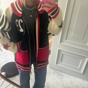 Stickad cardigan jacka med stjärnor - Säljer en oversized stickad cardigan jacka med dragkedja, i beige, svart och rött. Jackan har coola stjärnor och ränder på ärmarna, bred krage och fickor framtill. Perfekt för dig som gillar statement-plagg och sportig vibe. Nytt 1400❤️