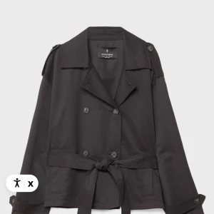 Svart trenchcoat från Stradivarius  - Snygg svart trenchcoat från Stradivarius i storlek S. Jackan har dubbelknäppning, klassisk krage, axelklaffar och bälte i midjan. Tillverkad i ett slätt tyg med knappar på ärmsluten för extra detalj. Perfekt för dig som gillar stilrena och tidlösa plagg. Kommer tyvärr INTE med det tillhörande bandet då jag har slarvat bort de