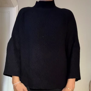 Svart stickad tröja - En svart stickad tröja med hög hals och en avslappnad passform. Tröjan har vida, raka ärmar och är ribbad för en snygg look. Storlek L men lite liten för mig på ärmarna.