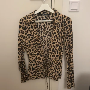 Leopardmönstrad blus från Zara XS - Säljer en snygg leopardmönstrad blus från Zara i storlek XS. Blusen har lång ärm, krage och knytning framtill som ger en cool och trendig look. Färgerna går i beige, brunt och svart och materialet känns mjukt och följsamt.